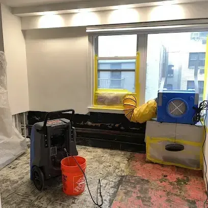 A dehumidifier and an air mover set up in a room where the flooring has been taken up