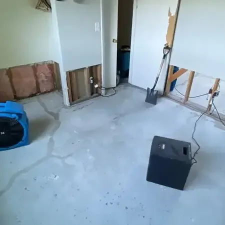 Air movers and a dehumidifier in a room with the lower drywall removed and bare floor showing