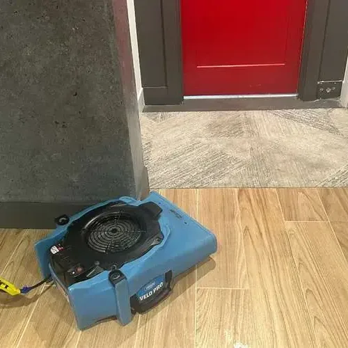 Single air mover blowing across a wood-look tile floor beside an open doorway during drying