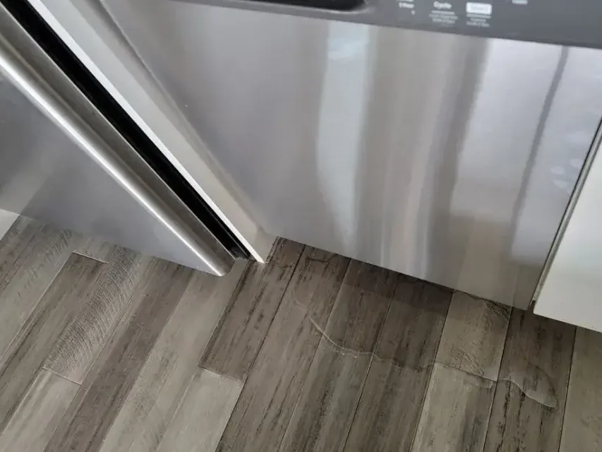 Leaked water pooled on plank flooring in front of a dishwasher